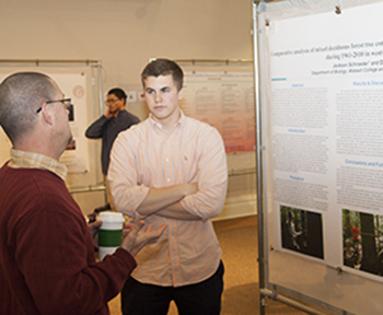 Jackson Schroeder '15 (right) ponders a point during his poster presentation.
