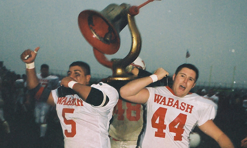 two men in football uniforms holding a trophy