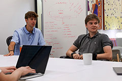 Adam Gaskill '27 (left) and Kyle Foster '27 listen to a colleague at the Nomad Coworking Space in Indianapolis during their summer internship with REVelry, a sales accelerator that pairs Wabash undergraduates with early-stage companies for real and quantifiable work in sales and go-to-market engineering.