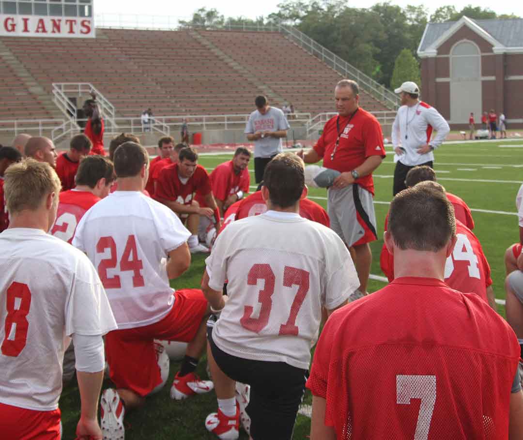 Head Coach Erik Raeburn talks to members of his 2012 football squad after an early season practice. 