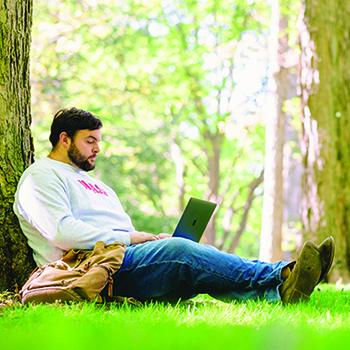 Jackson Miller ’23 sits under a tree with his laptop