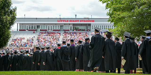 a group of graduates standing in a line in front of a stadium