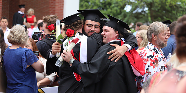 two men in graduation gowns and caps hugging