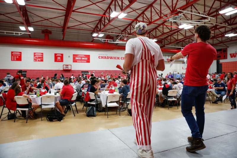 a man in a striped jumpsuit standing in a room with tables and chairs