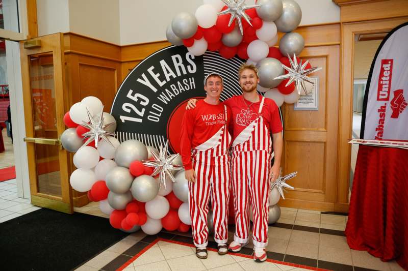 two men standing in front of a balloon arch