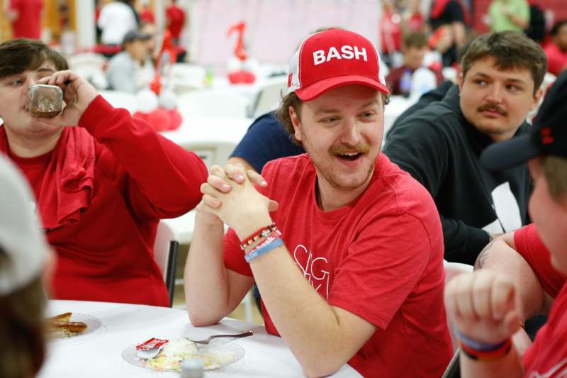 a man wearing red shirt and hat sitting at a table with other people
