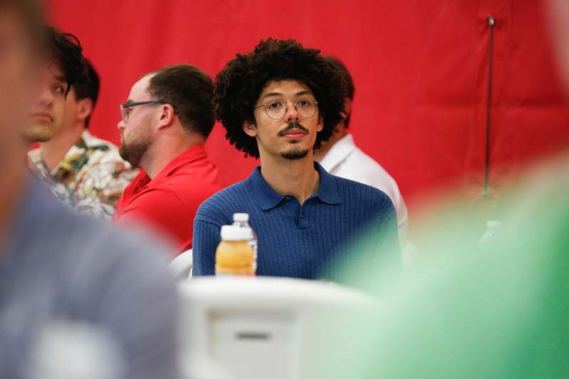 a man with curly hair and glasses sitting in a room with a red wall