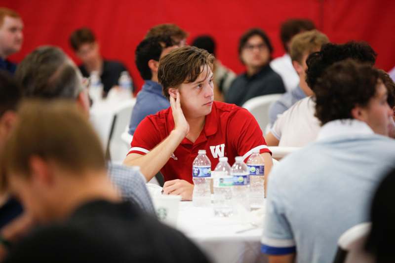 a man sitting at a table with water bottles and a red background
