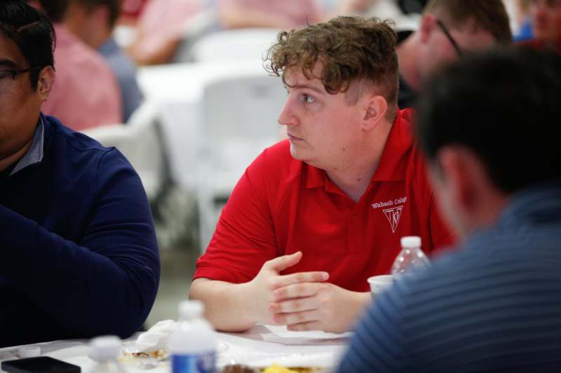 a man in a red shirt sitting at a table with other people