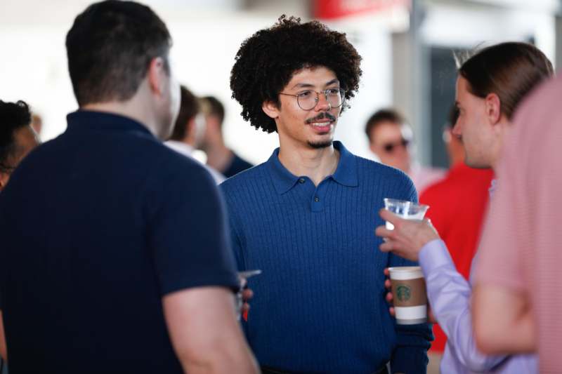 a man with curly hair and glasses holding cups of coffee
