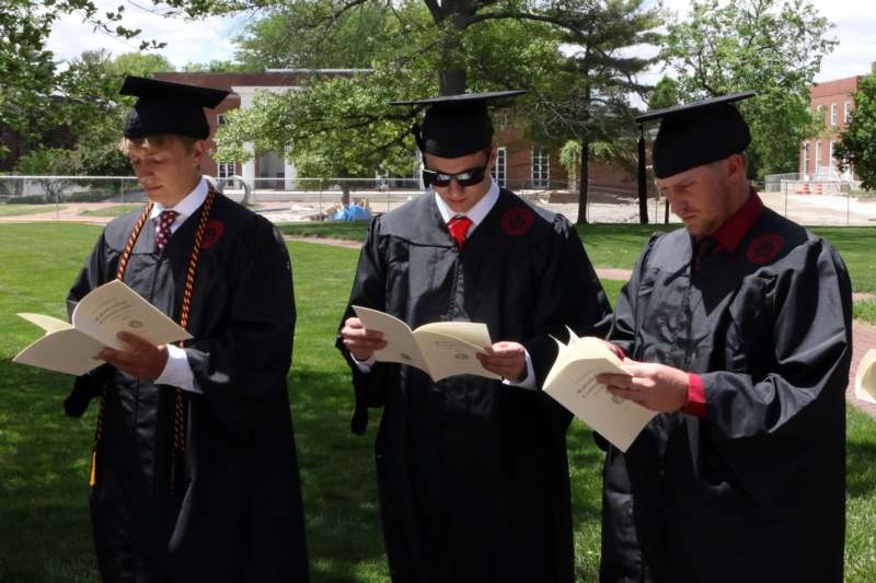 a group of men in graduation gowns and caps reading papers