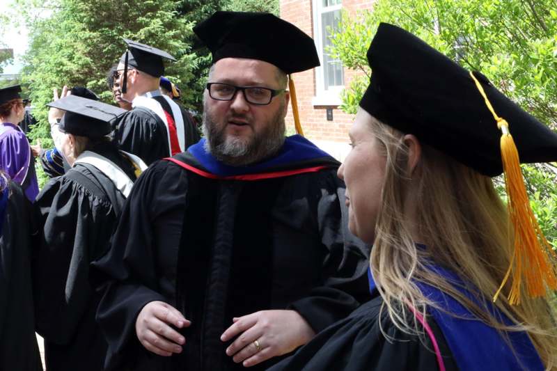 a man in a black robe and cap talking to a woman