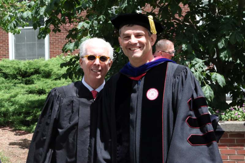 a man in a graduation gown and cap standing next to a man in a cap and gown