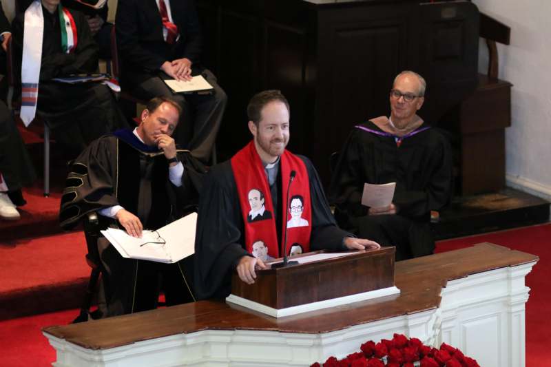 a man in a robe standing at a podium with other men in robes