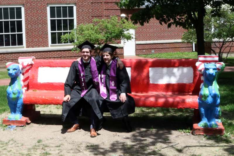 two men in graduation gowns and caps sitting on a bench