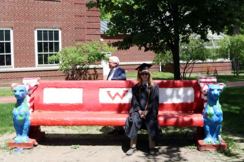 a woman in a graduation gown and cap sitting on a red bench