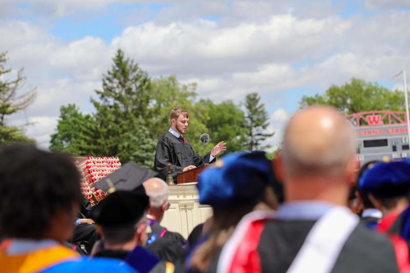 a man in a graduation gown speaking into a microphone