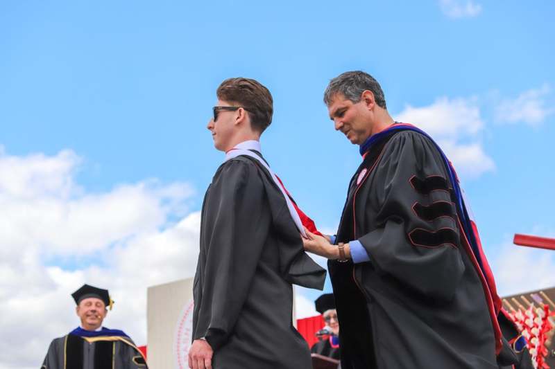 a man in black gowns and glasses standing next to a man in black gown