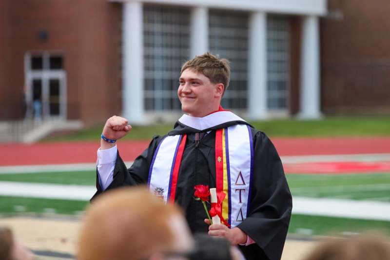 a man in a graduation gown holding a rose and a flower