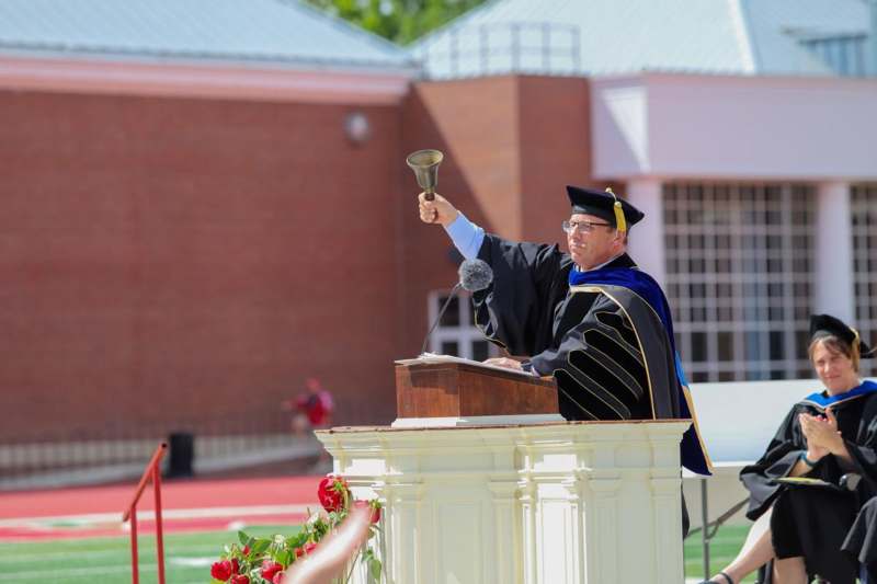 a man in a graduation cap and gown holding a bell
