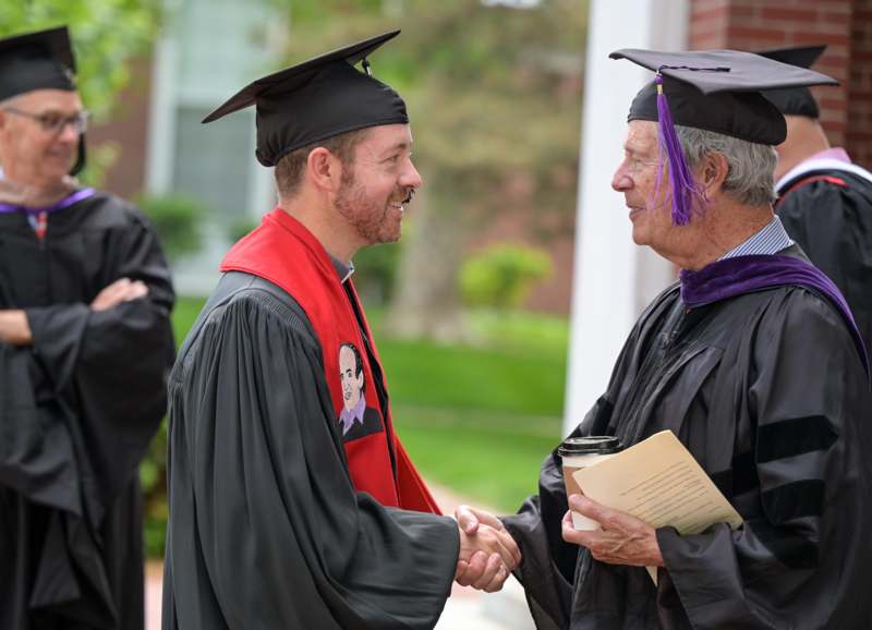 a man in a graduation gown shaking hands with another man
