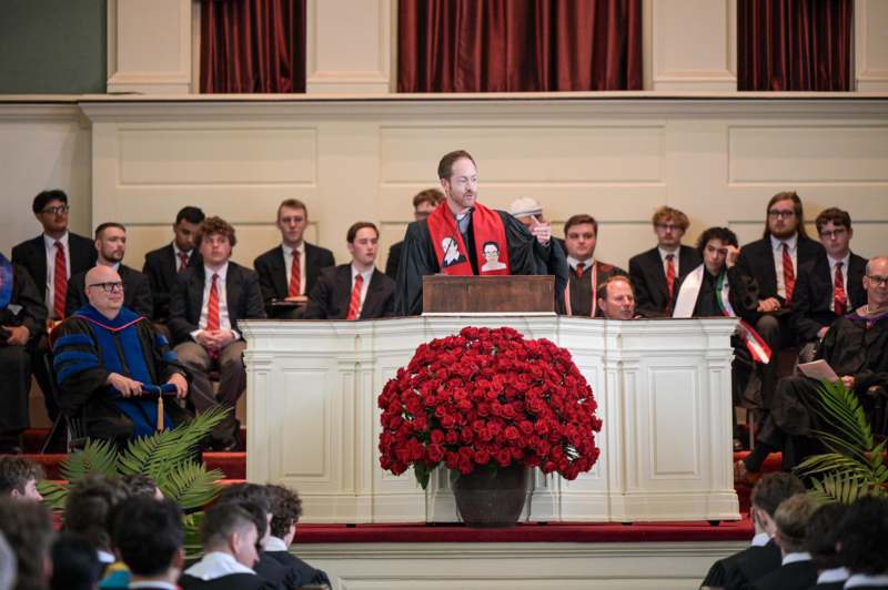 a man standing at a podium with a group of people in the background