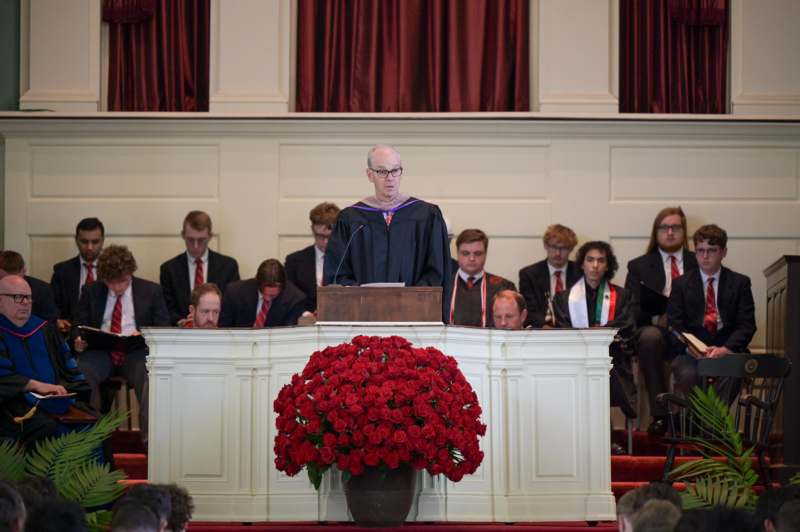 a man standing at a podium with a group of people in the background