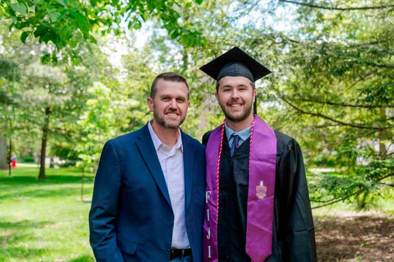 a man in a graduation gown and cap standing next to a man in a cap and gown