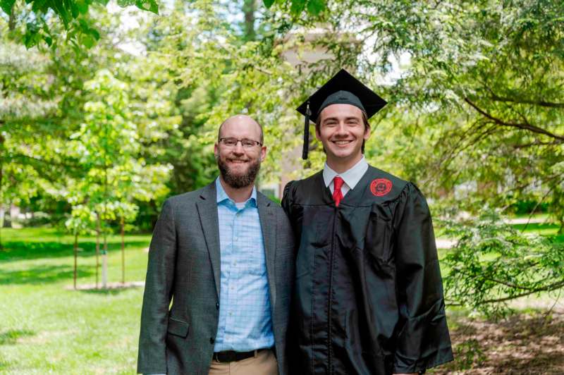 a man in a graduation gown and cap standing next to another man