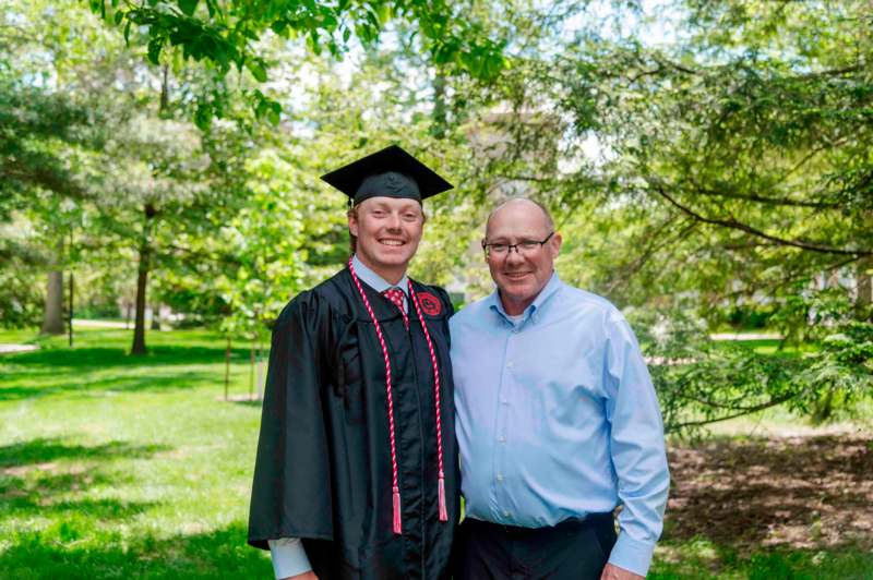a man in a cap and gown standing next to a man in a park