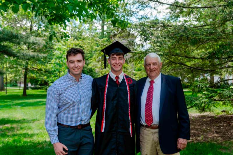 a man in a graduation cap and gown with a group of men in a park