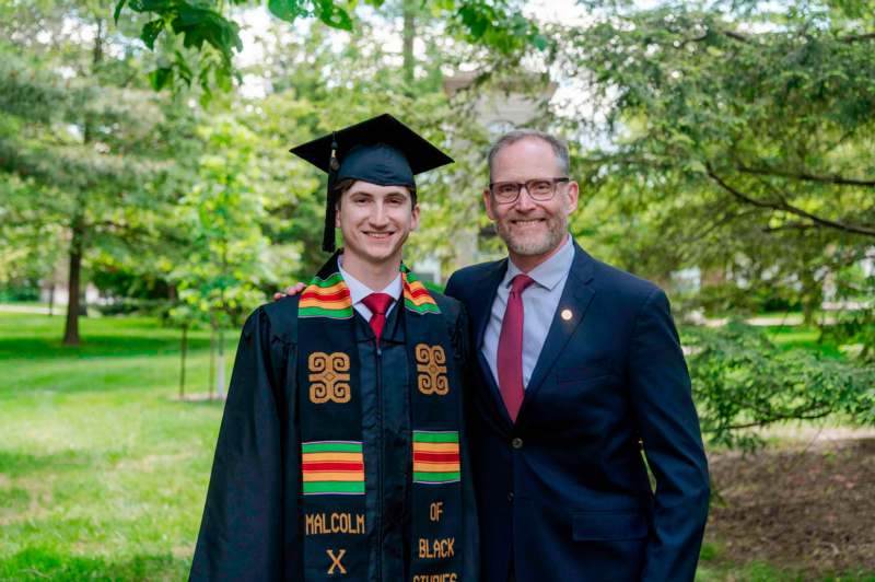 a man in a suit and cap standing next to a man in a graduation gown