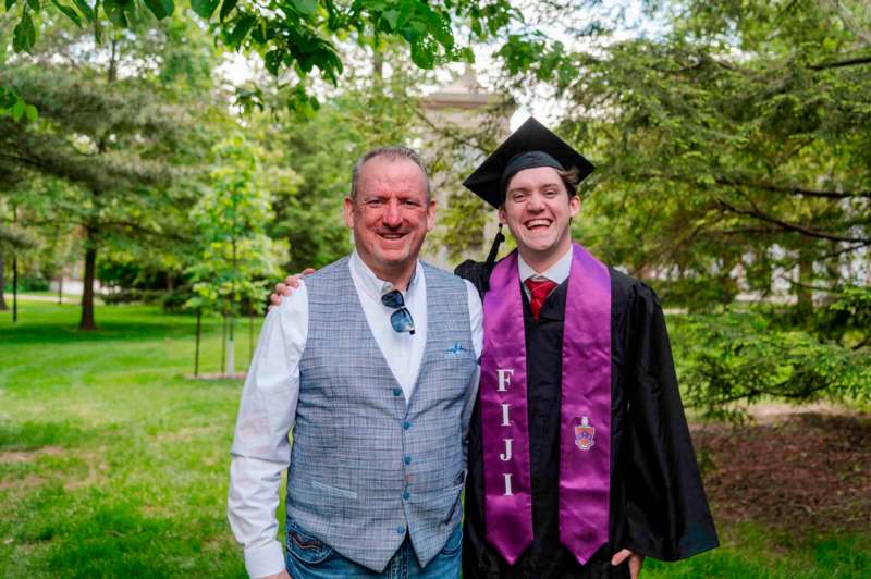 a man in a graduation gown and cap standing next to a man in a cap and gown