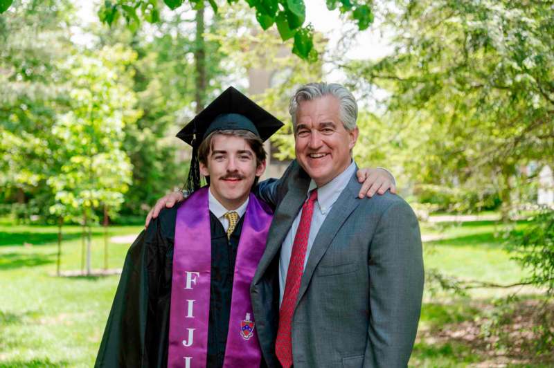 a man in a graduation gown and cap with his arm around a man