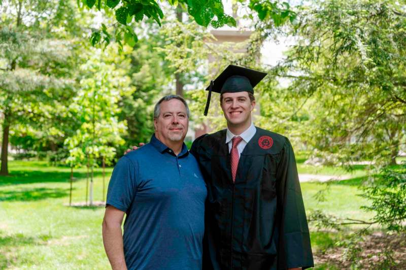 a man in a graduation gown and cap standing next to a man in a cap and gown