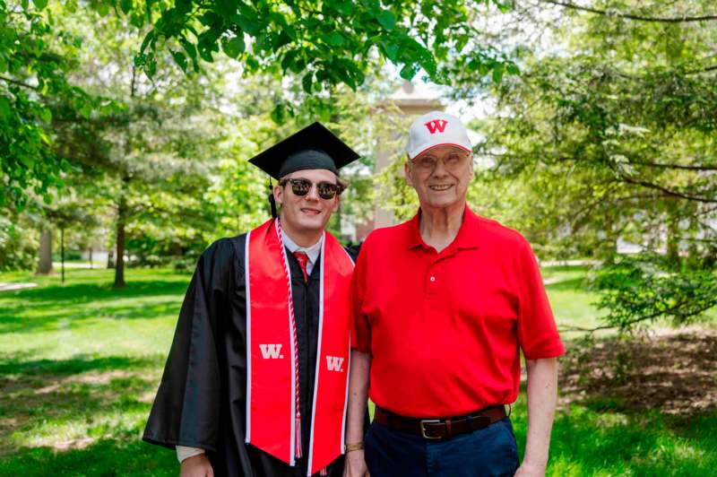 a man in a graduation gown and cap standing next to a man in a cap