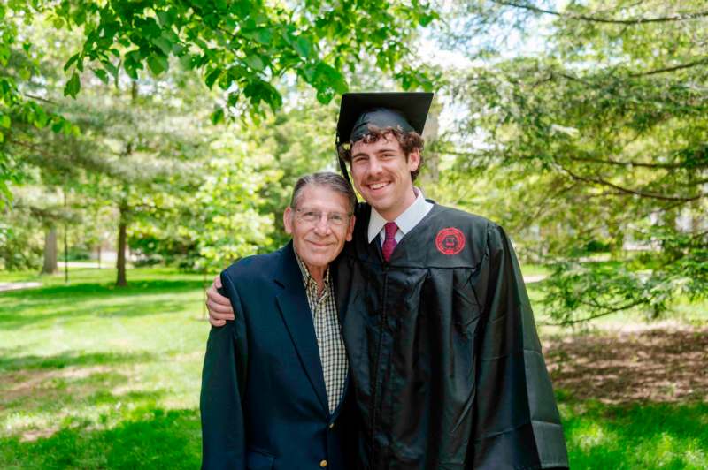 a man in a graduation gown and cap standing next to an old man