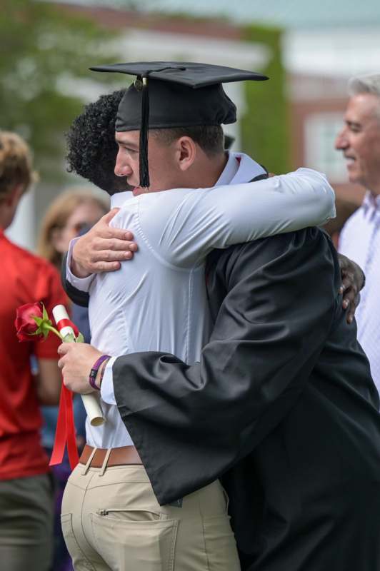 a man in a graduation gown hugging another man