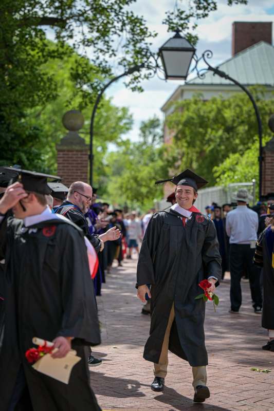 a man in a graduation gown and cap walking down a sidewalk