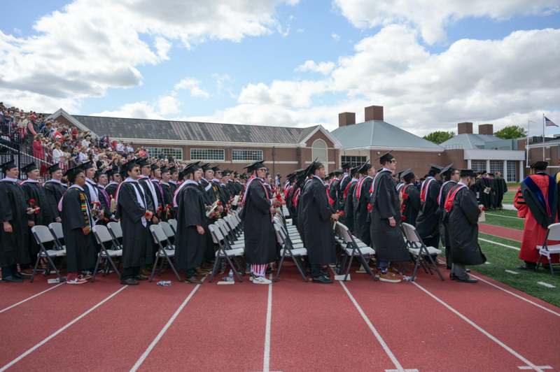 a group of graduates in black gowns and caps standing in chairs on a track