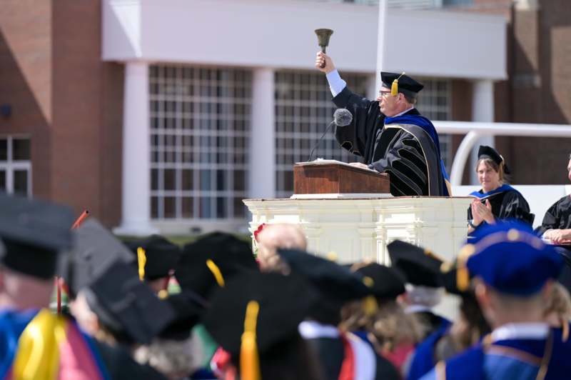 a man in a graduation gown holding a bell