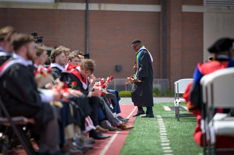 a man in a graduation gown holding a flower