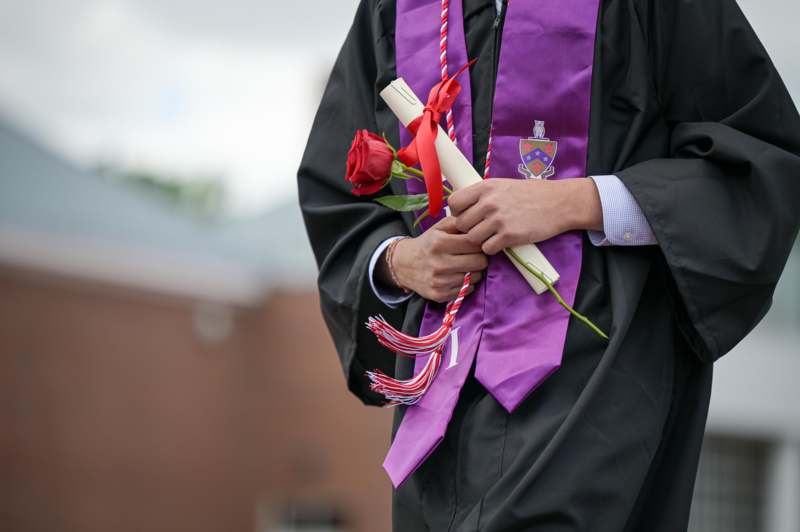 a person wearing a graduation gown holding a rose and diploma