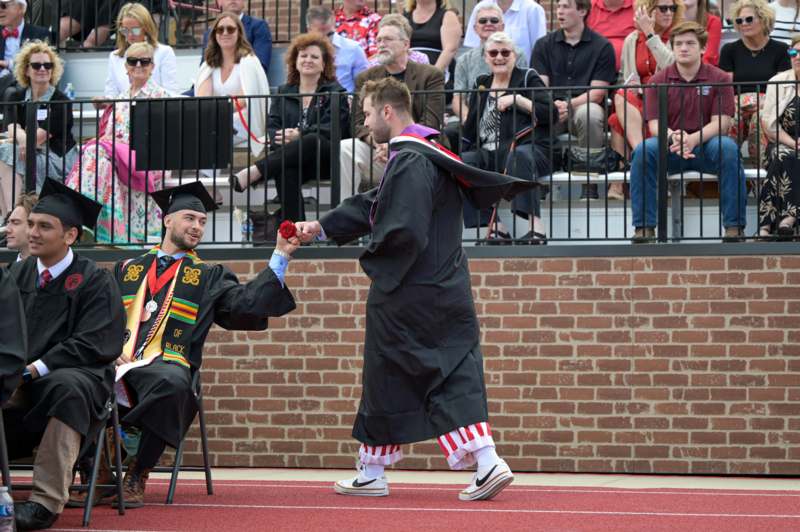 a man in a graduation gown giving a rose to another man