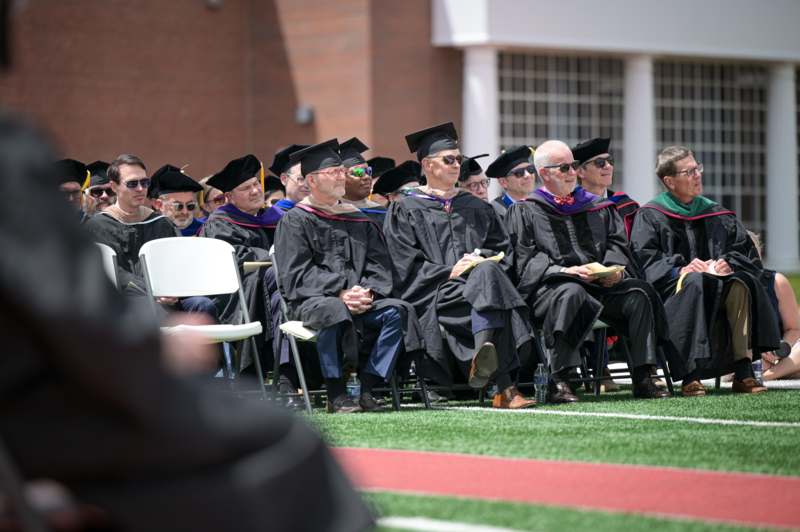 a group of people in graduation gowns and caps sitting in chairs