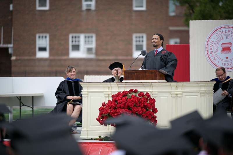 a man in a graduation gown speaking into a microphone