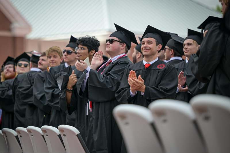 a group of people in graduation gowns and caps clapping