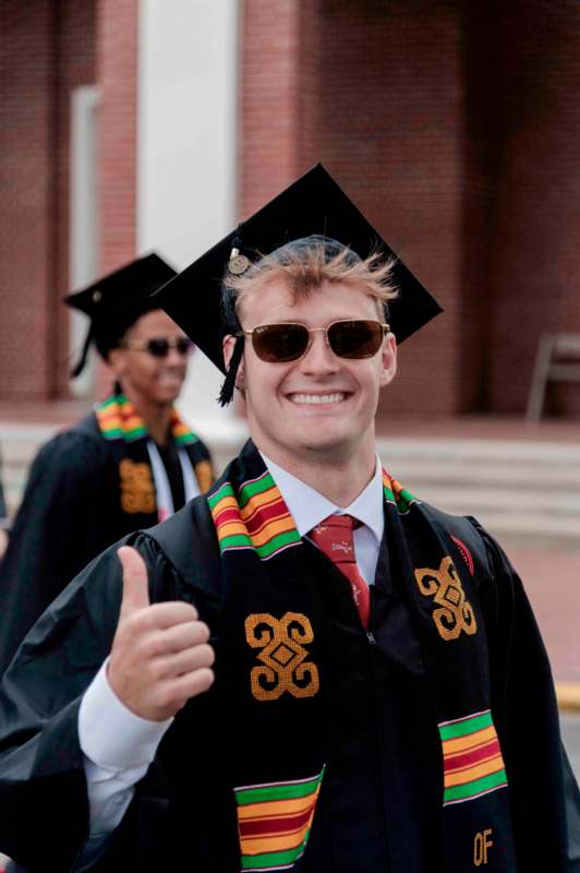 a man wearing a graduation gown and cap and gown giving a thumbs up