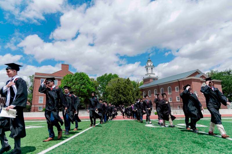 a group of people in black graduation gowns and caps on a football field