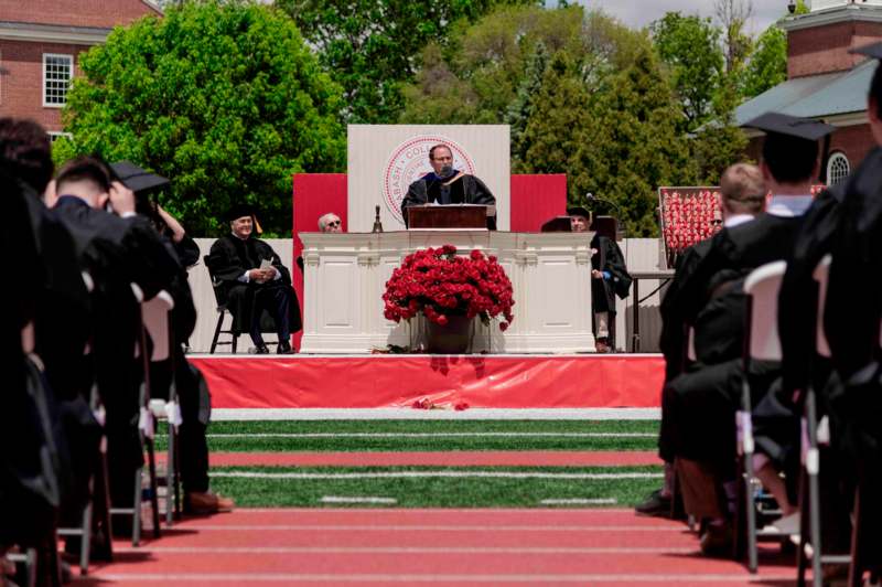 a man in a cap and gown standing at a podium with a group of people in the background